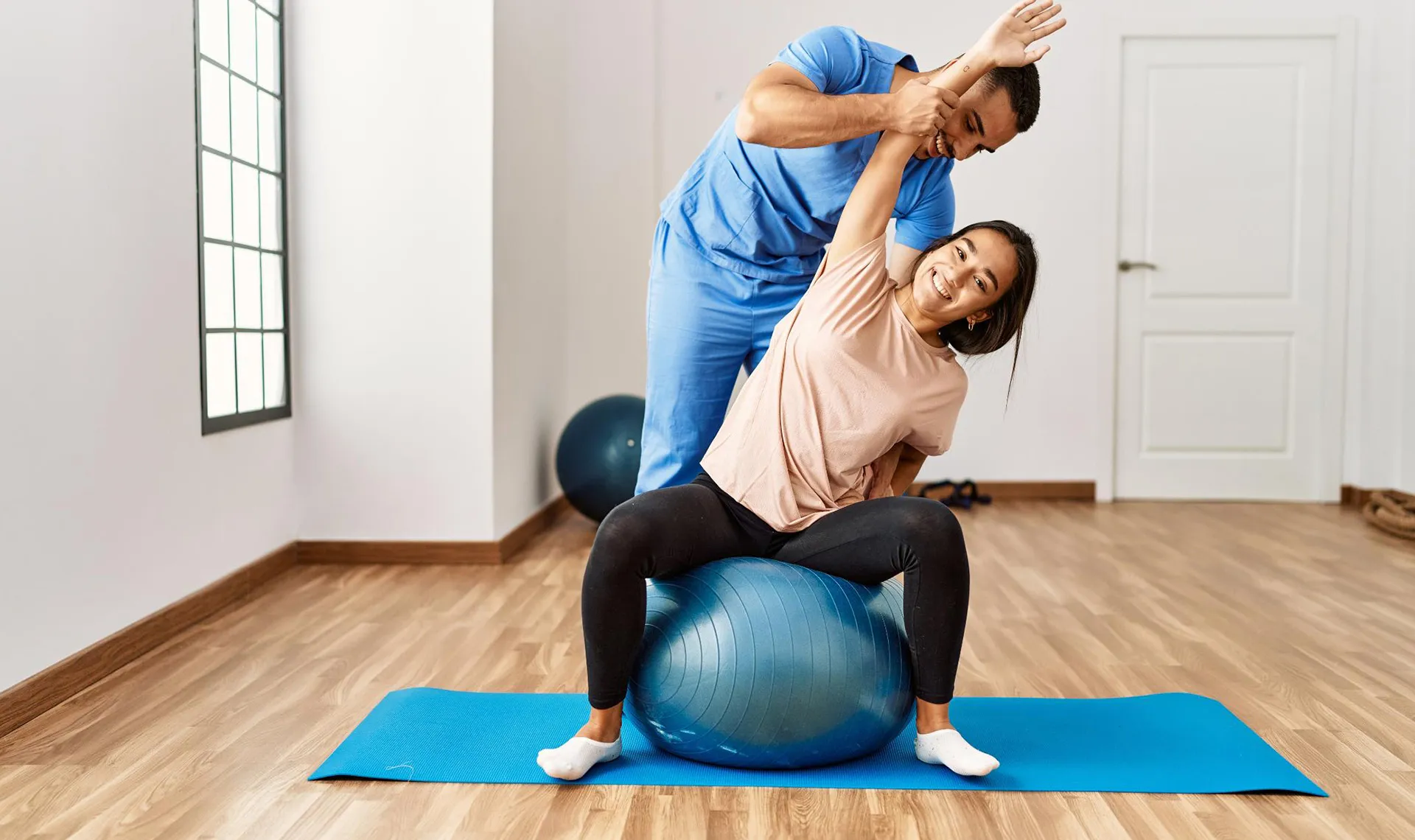 Bewegungstherapie im Reha-Zentrum Gro&szlig;gmain &ndash; Physiotherapeut unterst&uuml;tzt Patientin bei Dehn&uuml;bung auf Gymnastikball